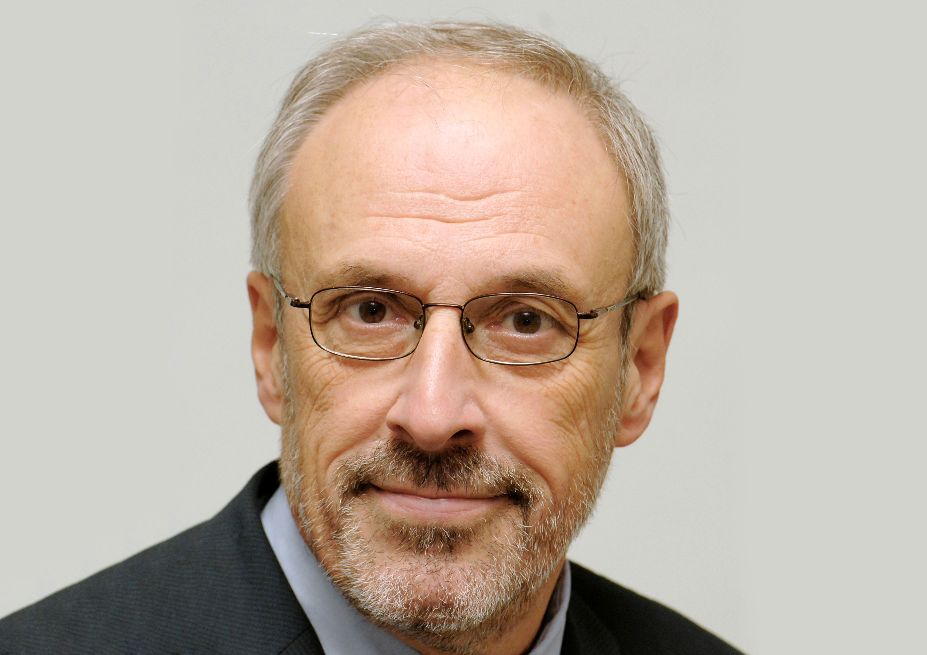 Portraitaufnahme eines Mannes mit silberner Brille und grauen Haaren vor hellem Hintergrund
